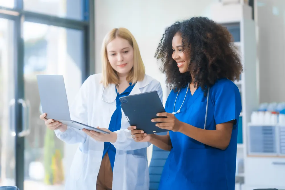Two healthcare professionals reviewing patient data on a laptop and tablet